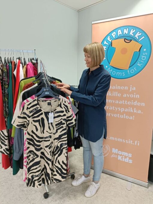 Vaatepankki-hankkeen koordinattori Kristiina Mäki selailemassa vaatetangolla olevia vaatteita.